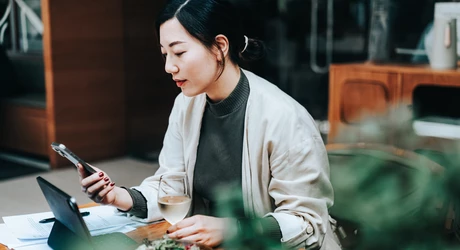 Person sitting at a table using a phone with a meal and drink nearby. 