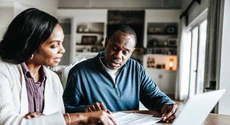 Husband and wife looking over bills and using laptop in kitchen. 