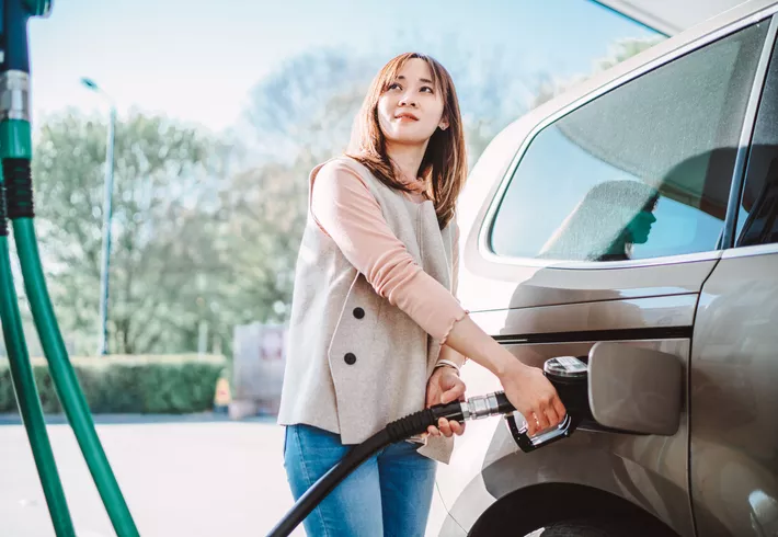 Woman fueling her vehicle at a gas station. 
