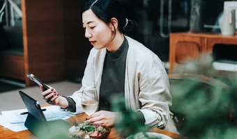 Person sitting at a table using a phone with a meal and drink nearby. 