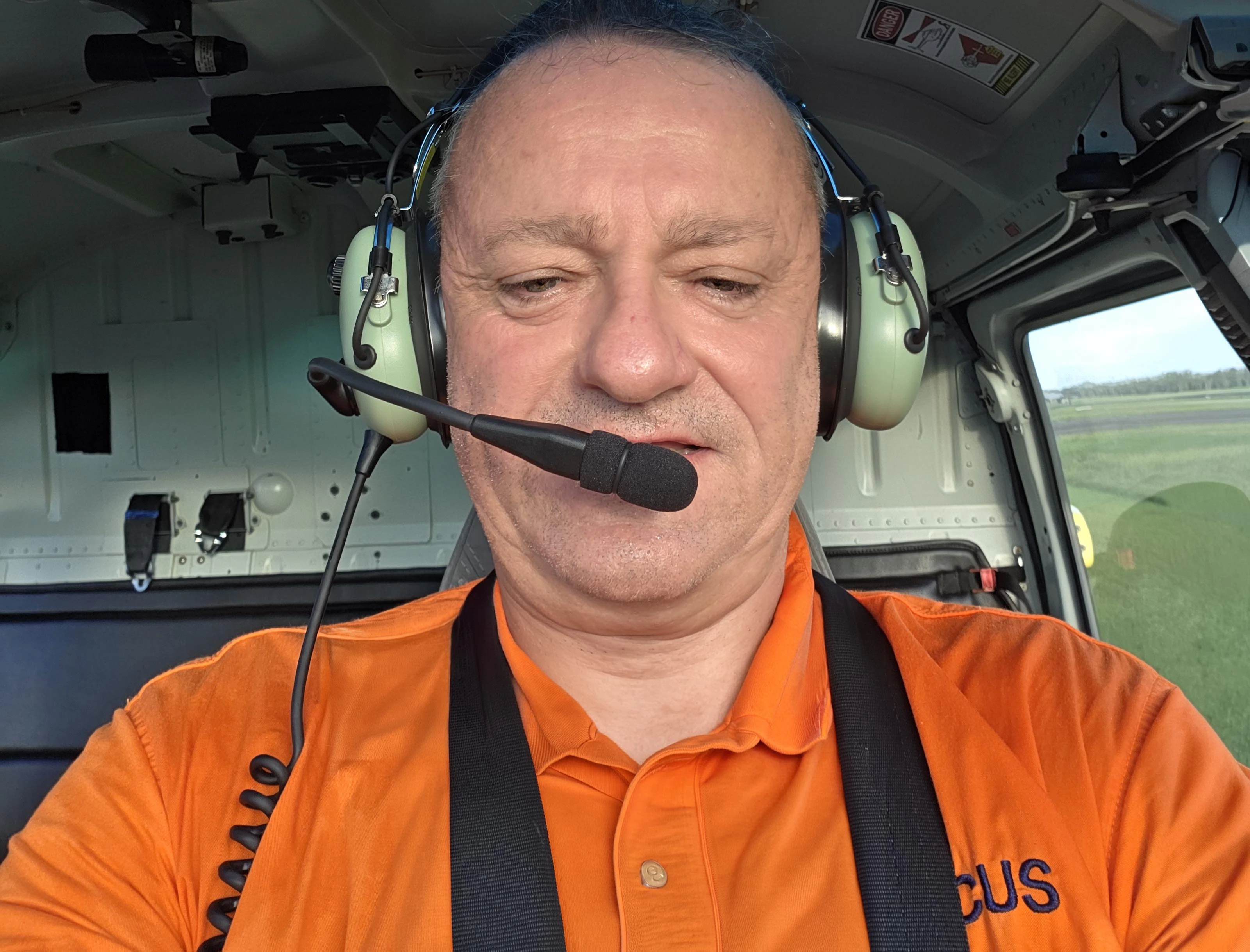 Vocus field technician Wayne in helicopter wearing an aviation headset and microphone and wearing an orange polo shirt with the Vocus logo on it. 
