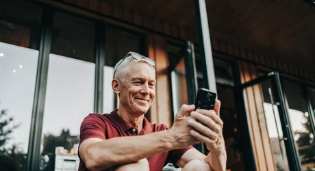 Mature man uses a phone while sitting on a sidewalk in summer 