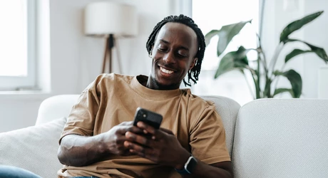 Smiling man sitting comfortably on a sofa while using a smartphone. 