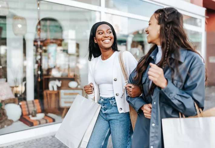 Two women friends walking and holding shopping bags. 