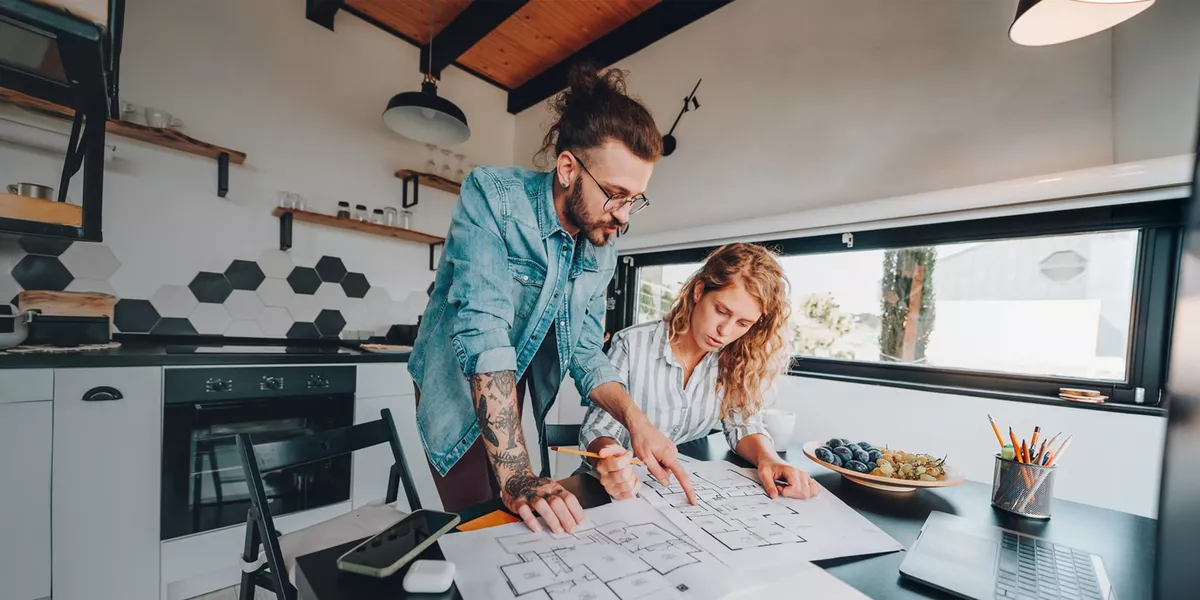 Two people review architectural plans together at a table in a modern kitchen.