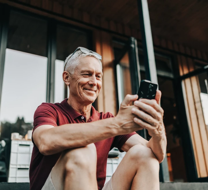 Mature man uses a phone while sitting on a sidewalk in summer 