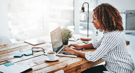 Professional African American woman sitting at her desk in brightly lit office working on laptop 