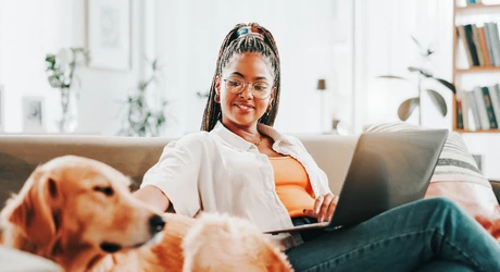 Smiling African American woman sitting on couch with her large dog and laptop 
