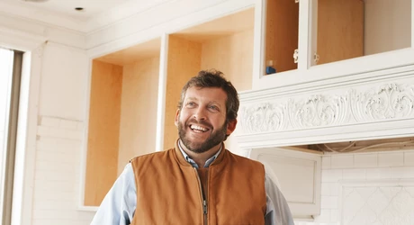 Smiling male builder wearing a construction vest, is inside a kitchen under construction. 