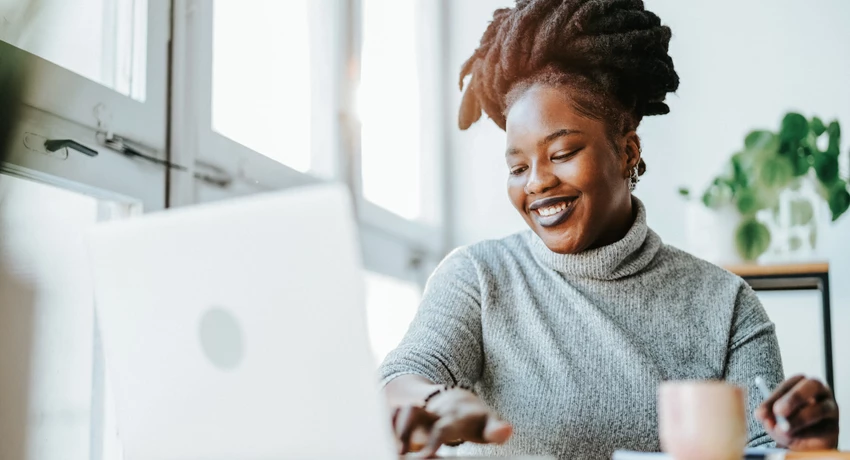 Smiling African American woman working on laptop in brightly lit office 
