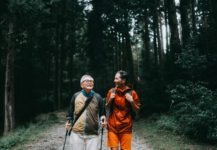 Senior father and adult son hiking in the forest. 