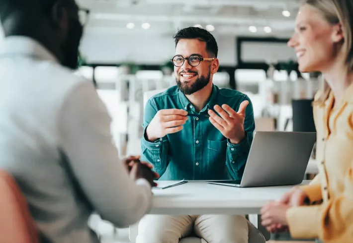 Friendly professional man gesturing with his hands to couple across the desk in office 