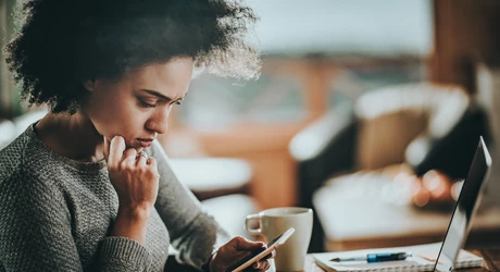  Young black woman reading a text message on her mobile phone while working at home. 