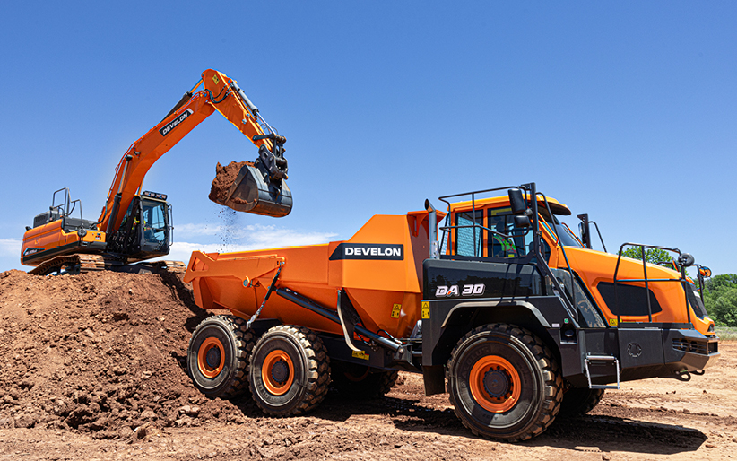 An excavator loads an ADT. Proper usage of machines can lead to a higher construction equipment resale value.