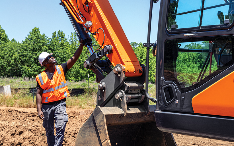 An operator inspects an excavator arm. Preventive maintenance can maximize construction equipment resale value.