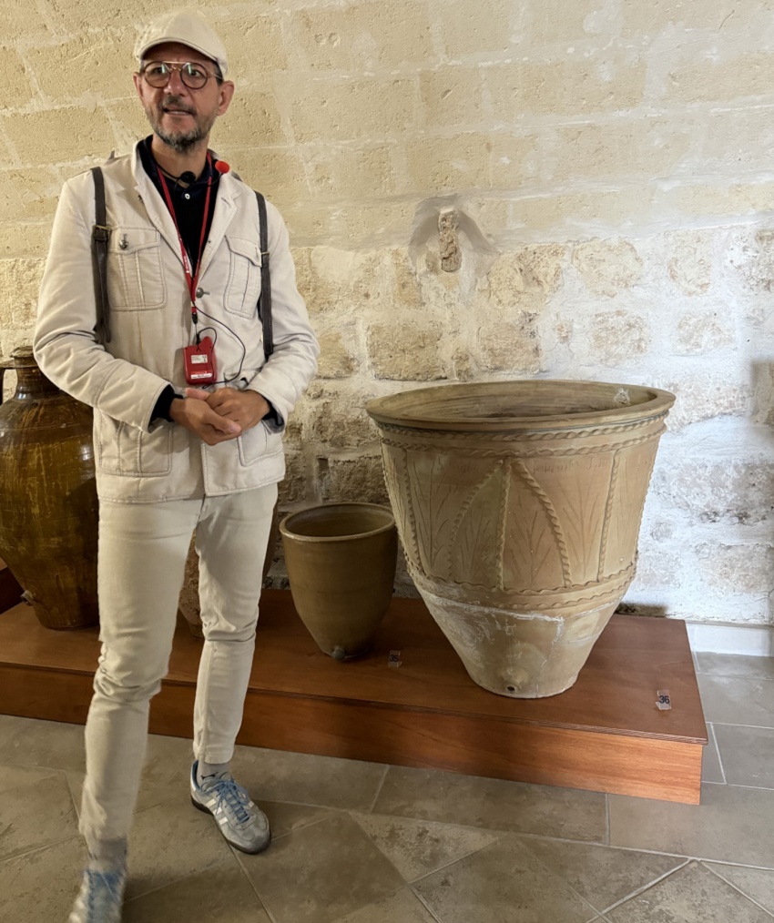 A group leader standing in front of a white stone wall with pottery in front of it