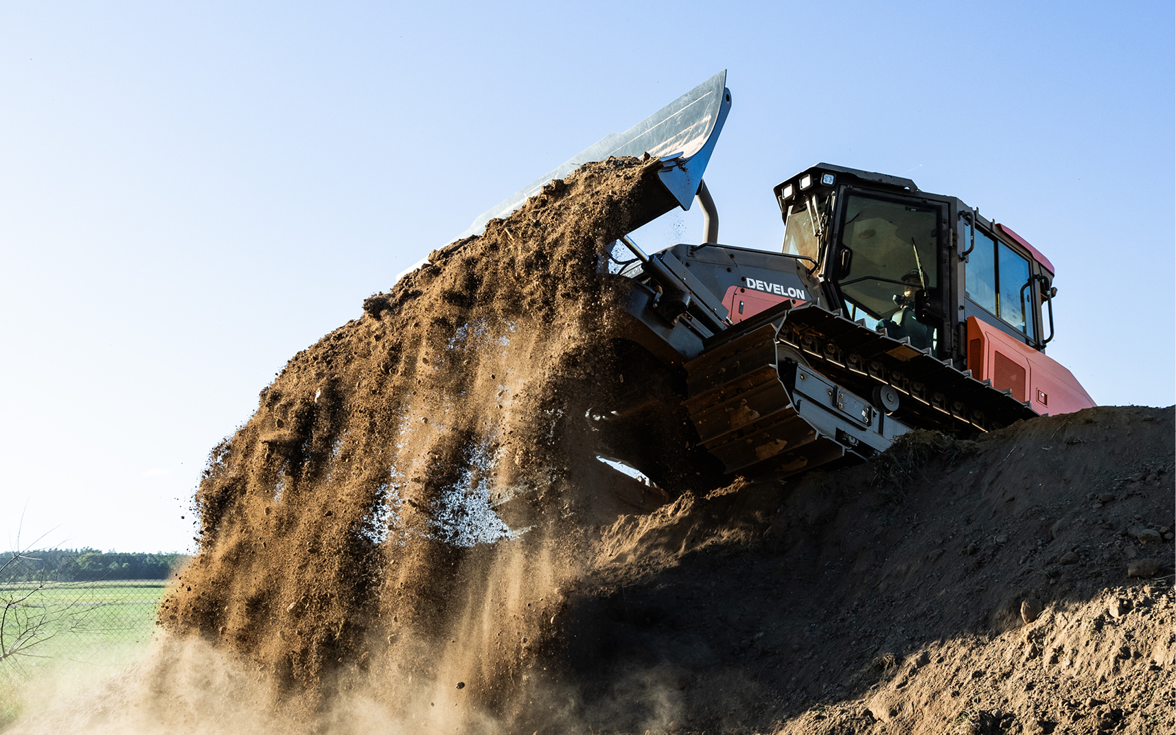 A DEVELON dozer pushing dirt with a large dozer blade.