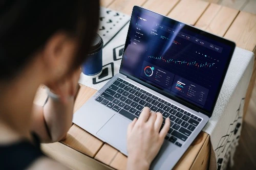 Over the shoulder shot of a woman on her laptop, looking at some graphs on her laptop's screen