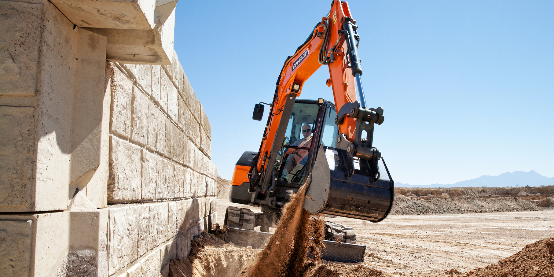 A DEVELON mini excavator works along a wall on a job site.