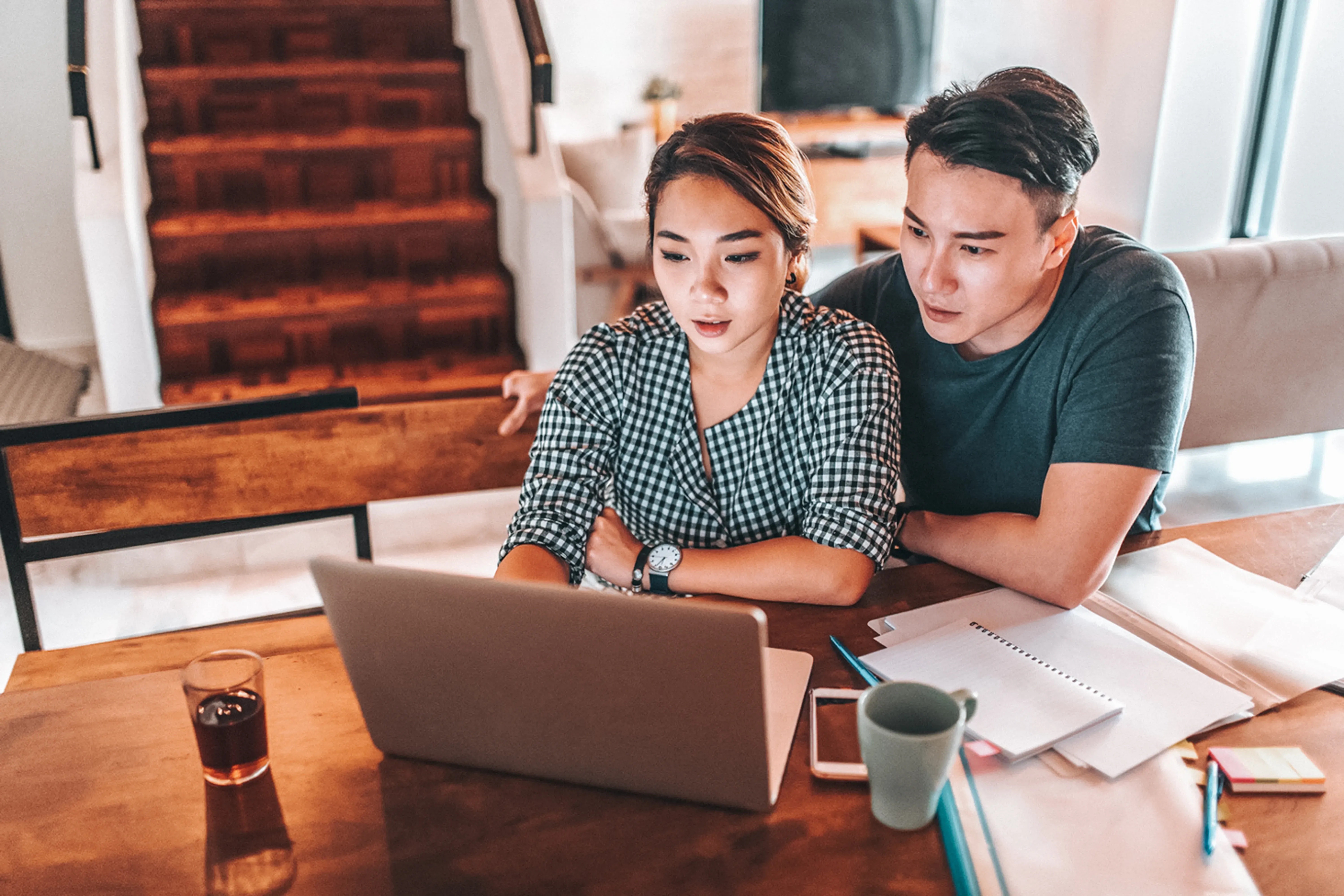 High angle view of couple sitting at dining room table with paperwork looking at laptop 