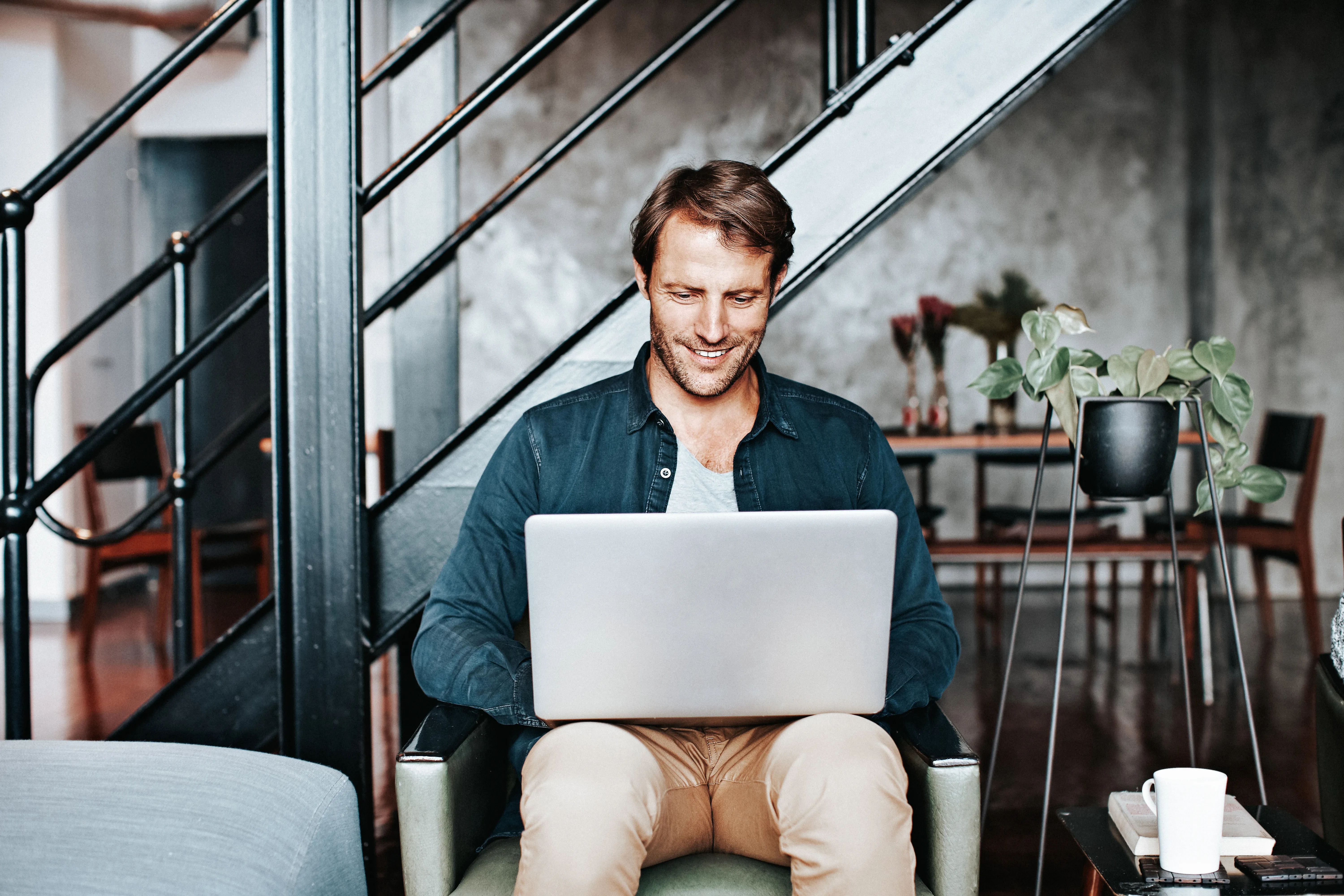 Man sitting on a chair in his living room using a laptop. 
