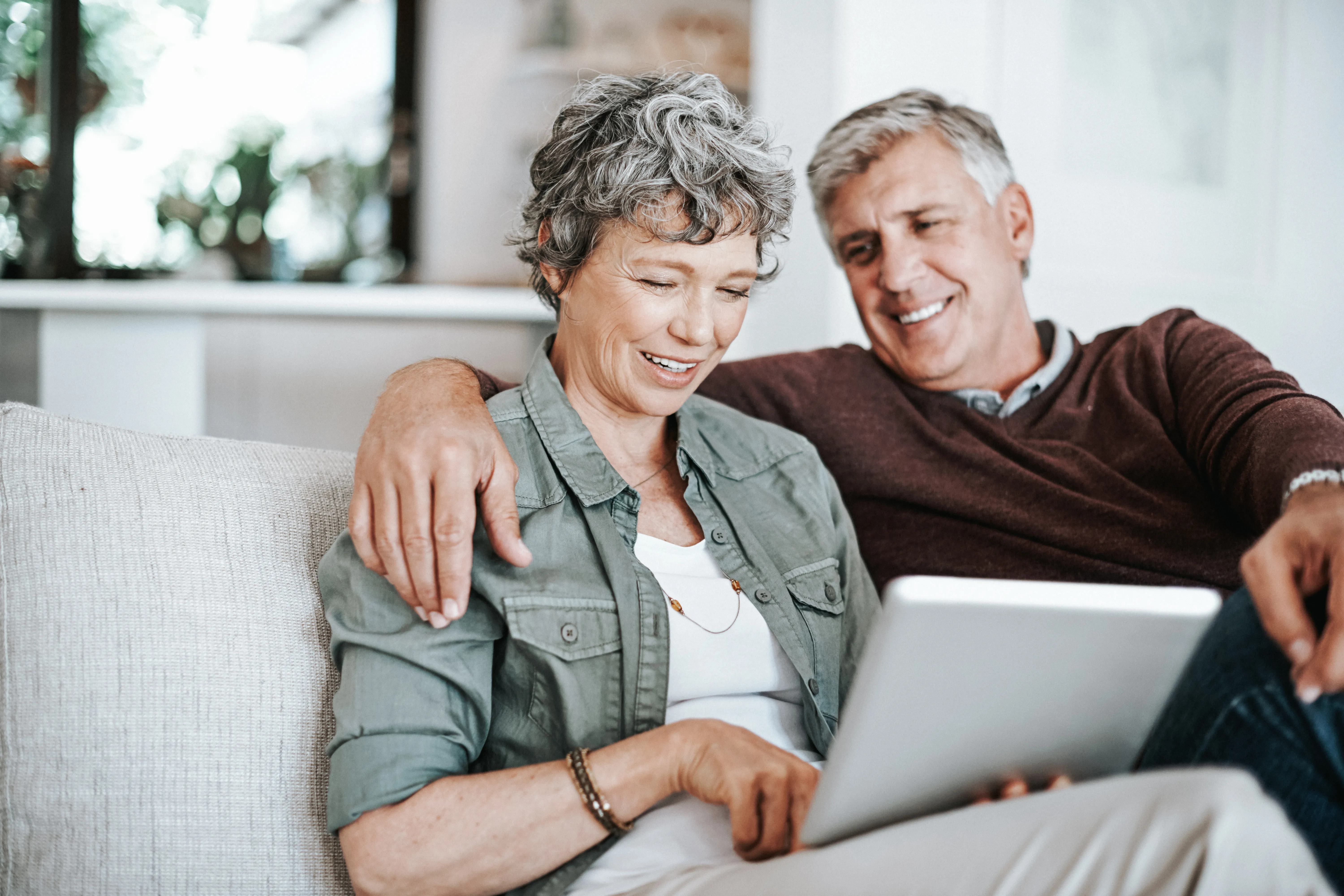 Mature couple using a tablet while relaxing on their sofa.