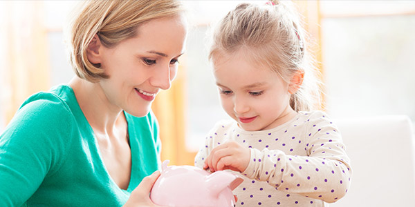 a mother holding a piggy bank while her daughter puts a coin in it