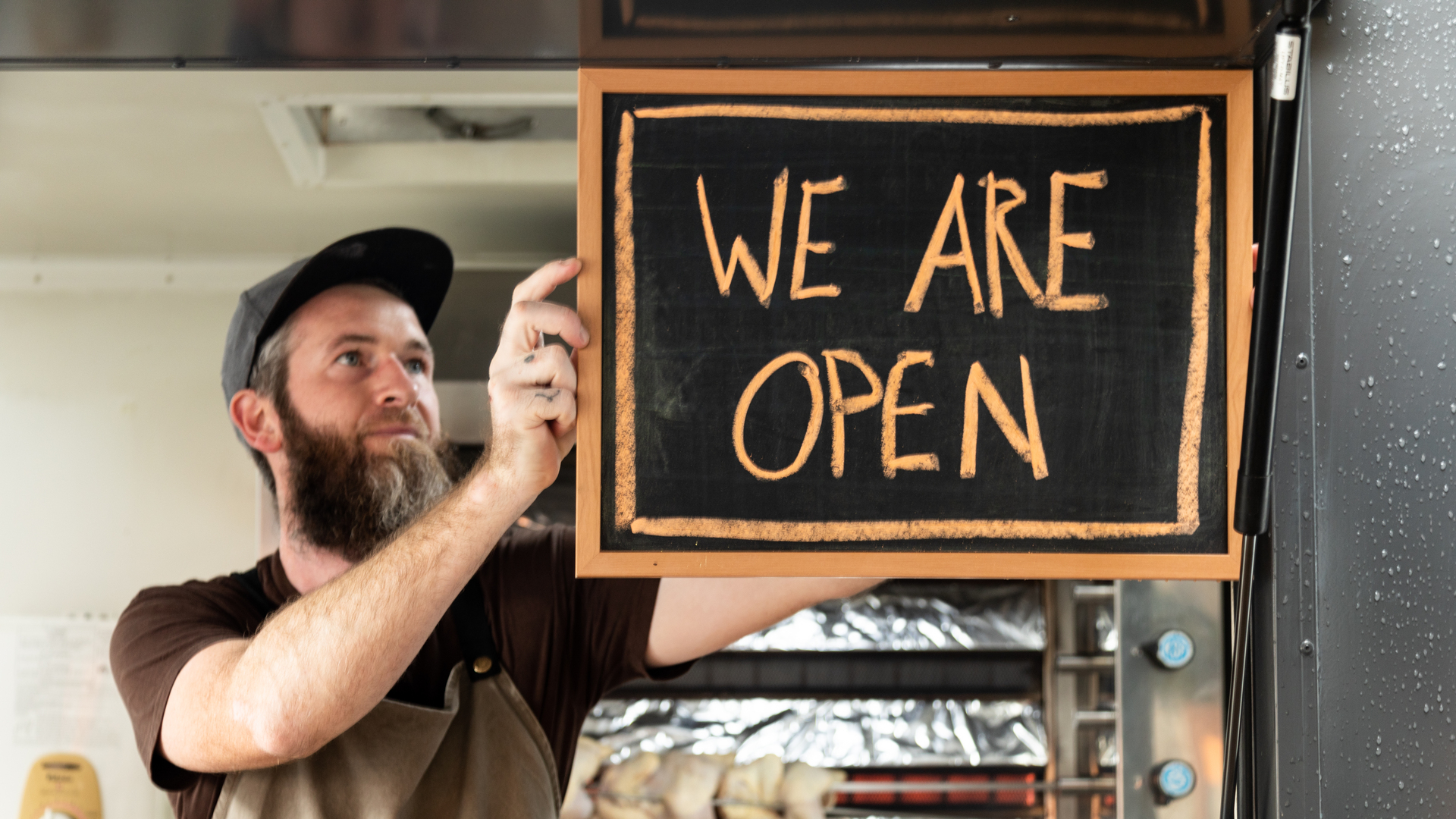 A Man holds a We Are Open sign as he opens his food truck for service