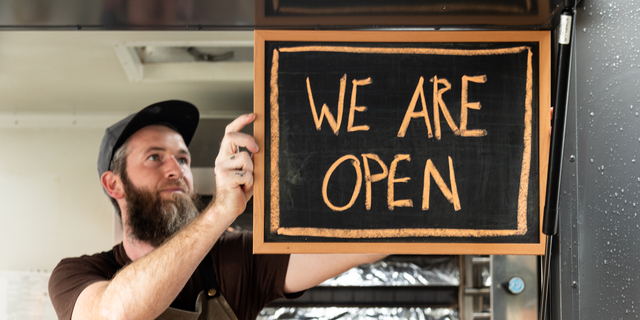 A Man holds a We Are Open sign as he opens his food truck for service