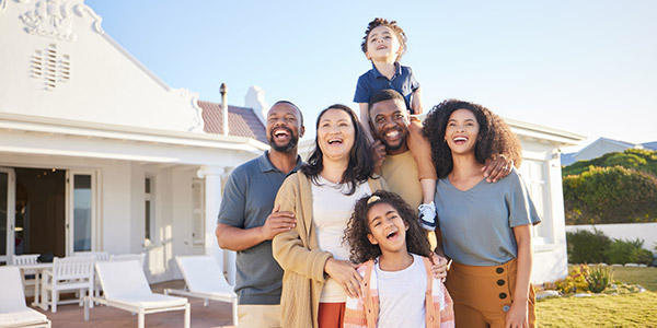 A happy mixed race family stands smiling in front of their home