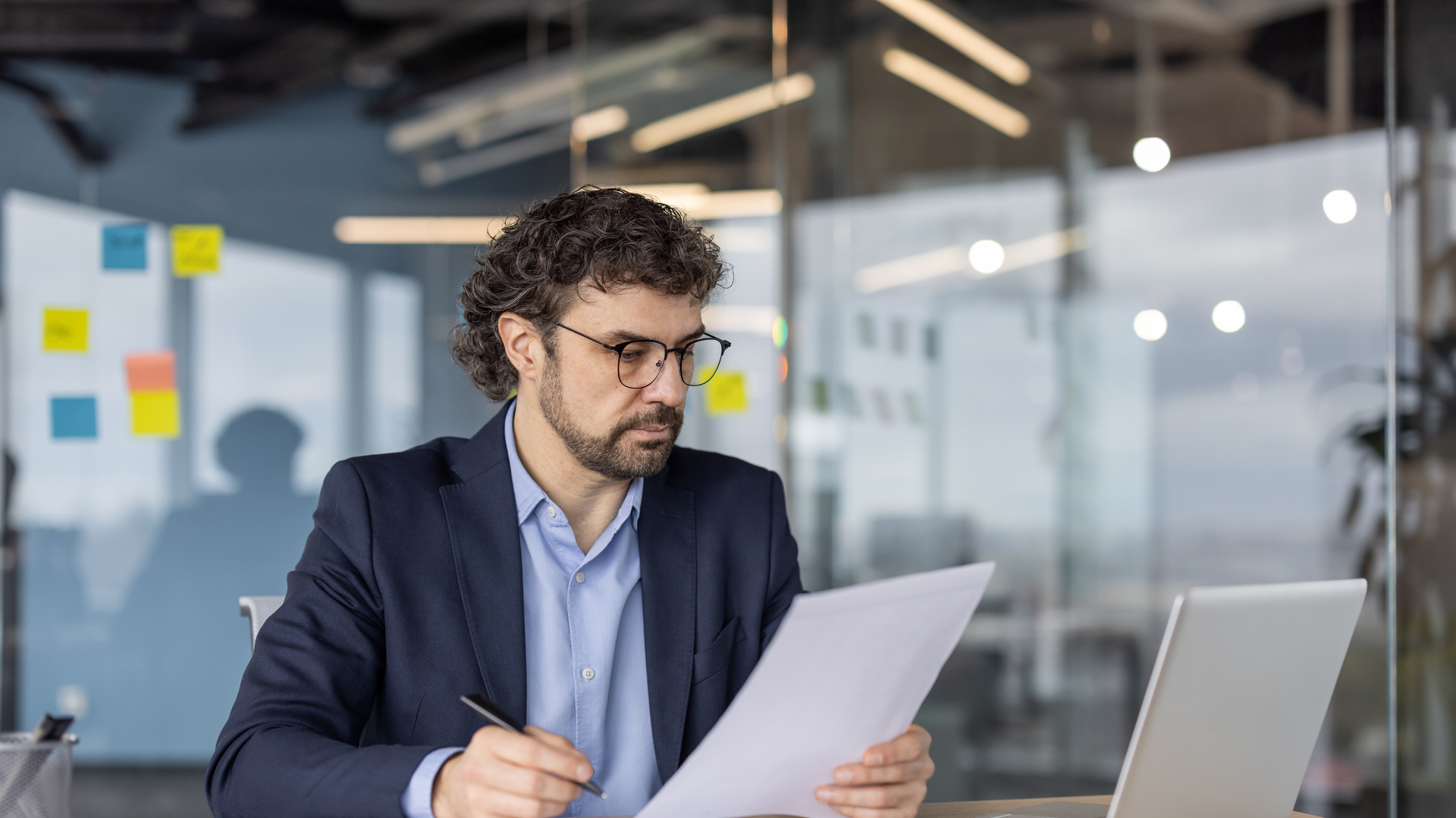 Serious businessman analyzing documents at office desk with laptop and papers