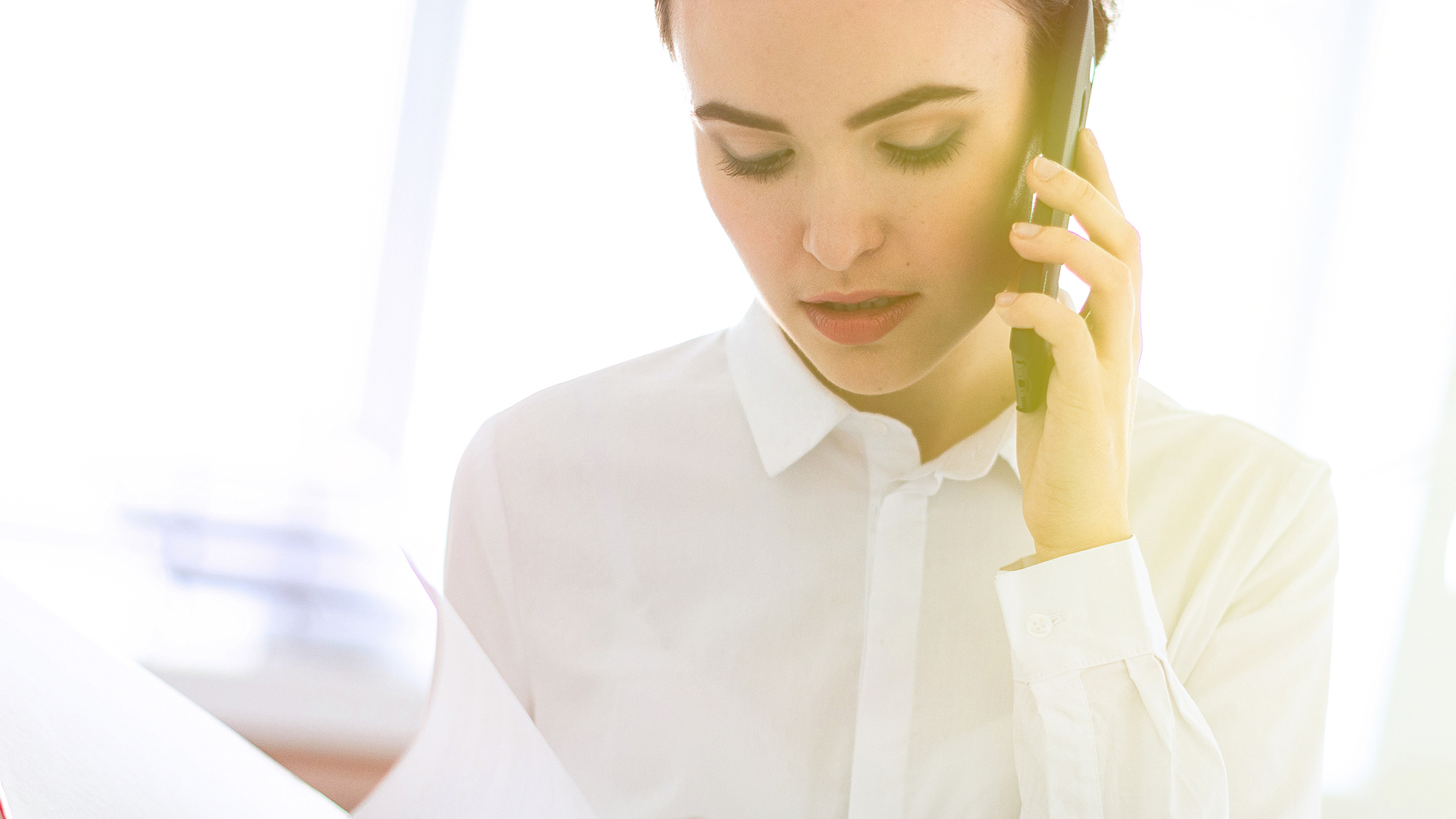 Young girl in the office near the rack and scrolls through the folder with the documents and speaks on the phone.