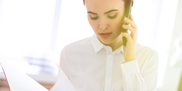 Young girl in the office near the rack and scrolls through the folder with the documents and speaks on the phone.