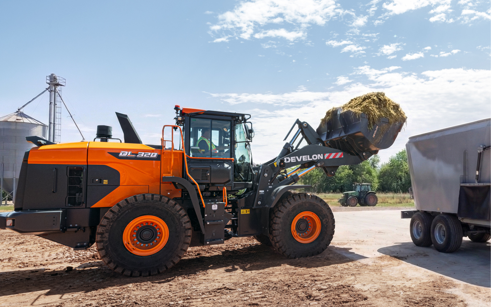 A DEVELON wheel loader lifts a bucket of silage for placement in a mixer.