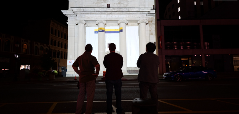 A group of people looking at a building light up at night with projection mapping.