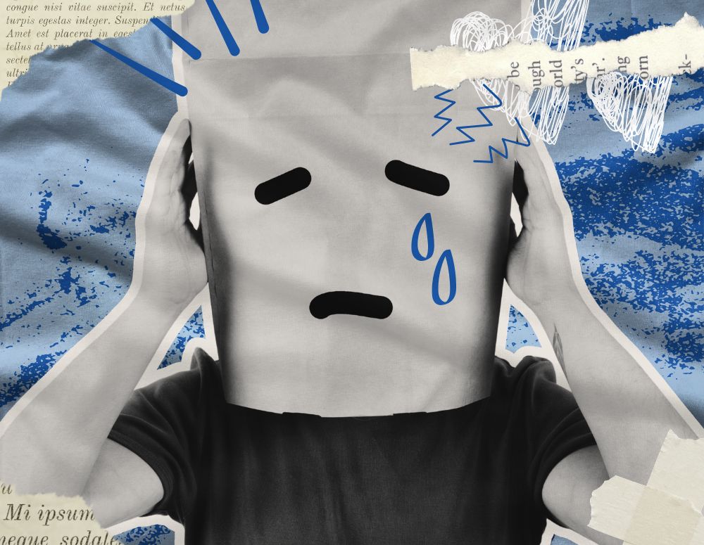 A boy wears a paper bag over his head with a sad face. Drawn on tears drip from his eyes.