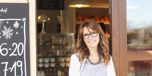 Small coffee shop owner standing in front of store.