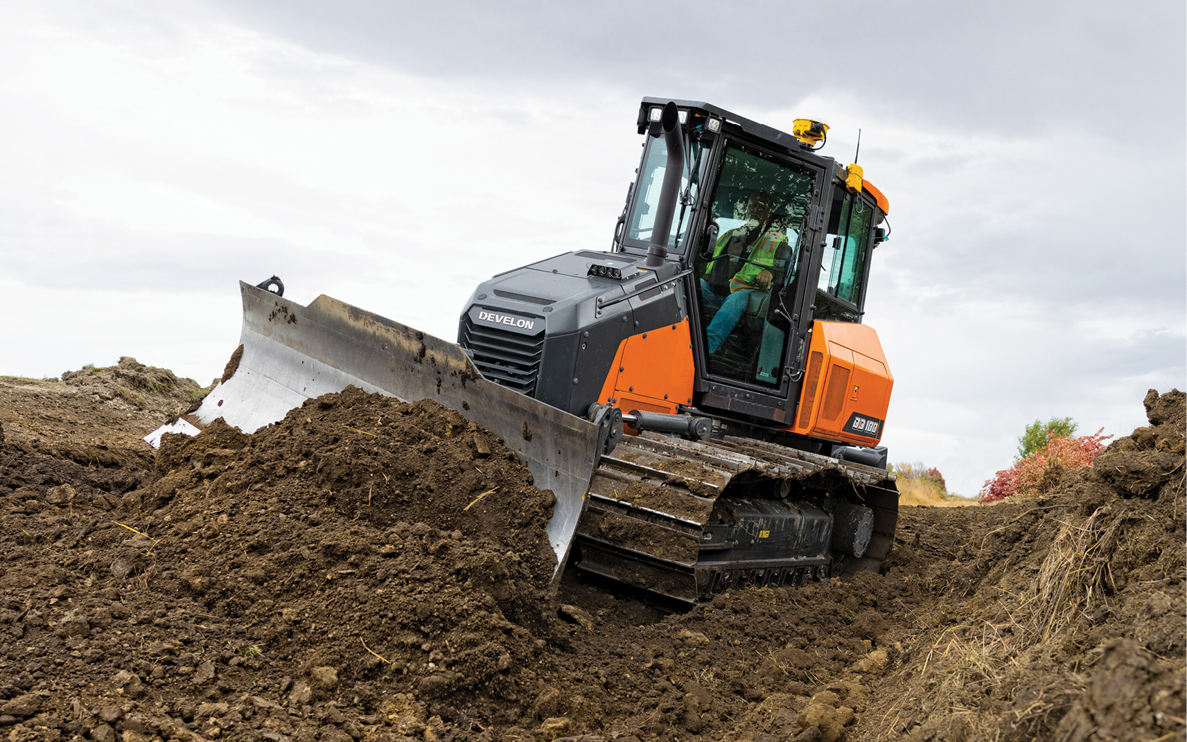 A DEVELON dozer pushes dirt on a job site with a grading blade.