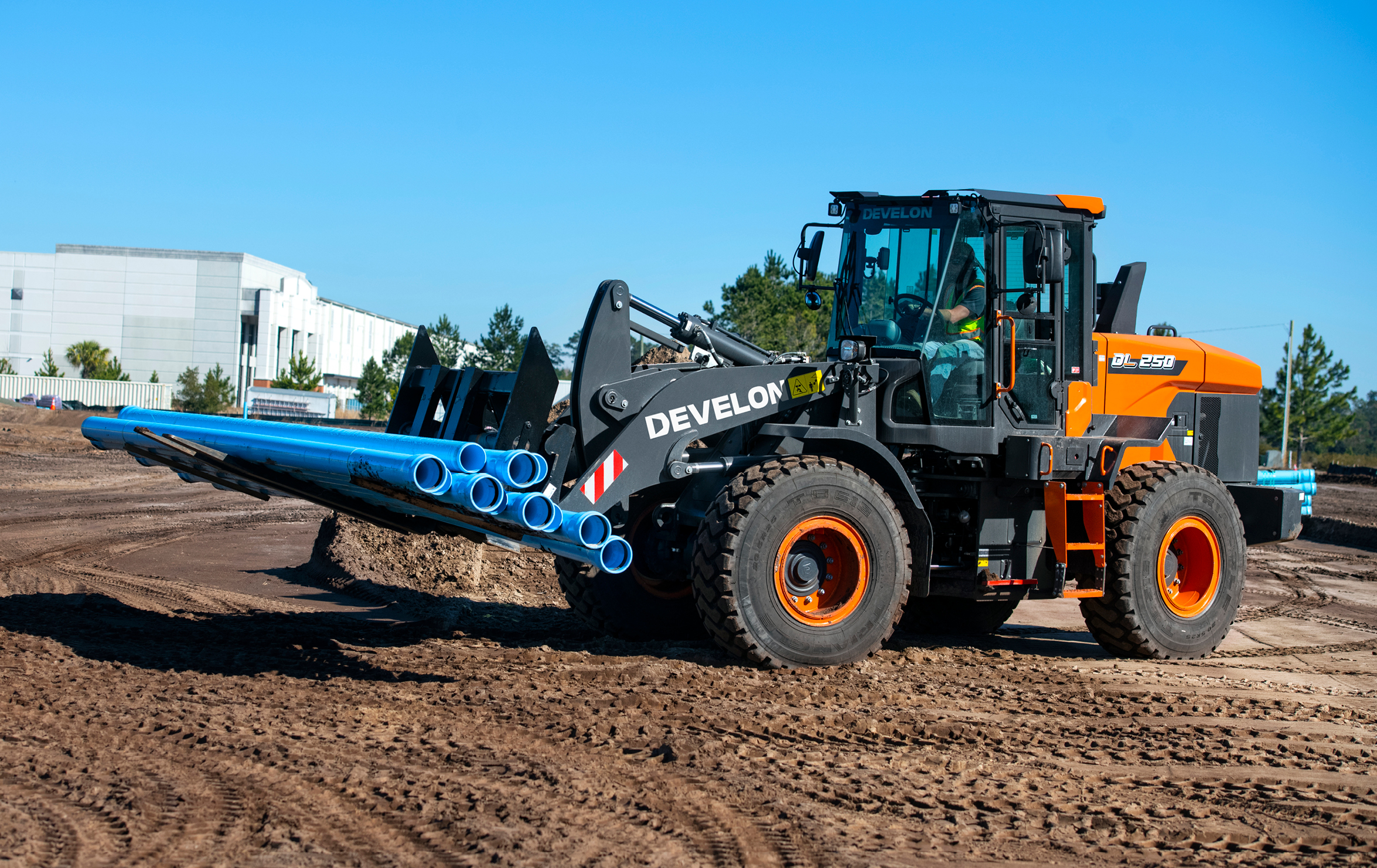 The DEVELON DX100W-7 mini wheel excavator hauls piping on a job site.