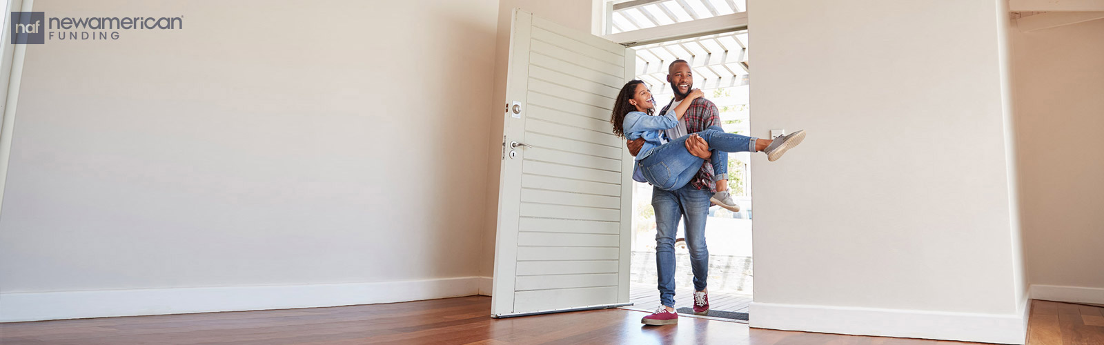 A Black man carries a smiling Black woman across the threshold of a new home