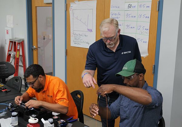 A BICSI instructor assists students holding fiber optic cabling during a hands-on technical training class