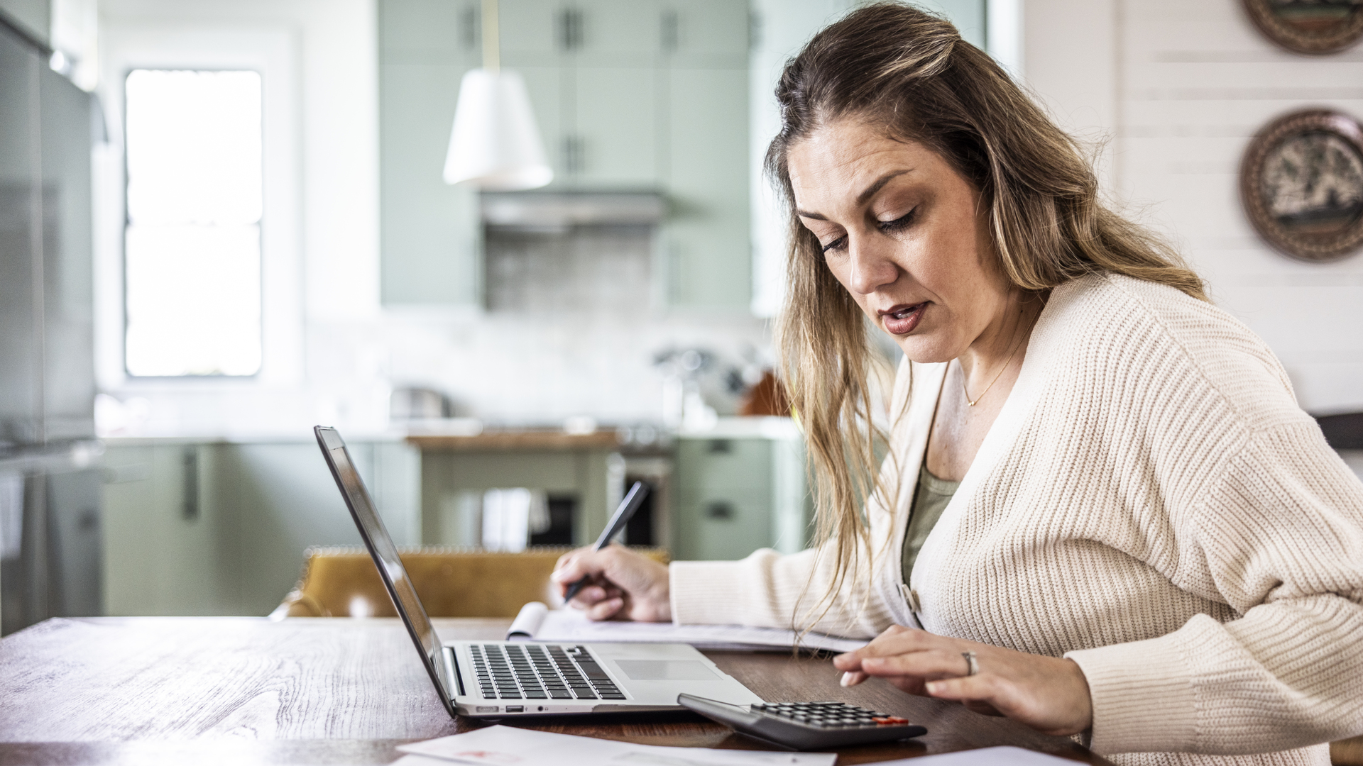 Woman paying bills with laptop at kitchen table