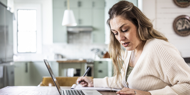 Woman paying bills with laptop at kitchen table