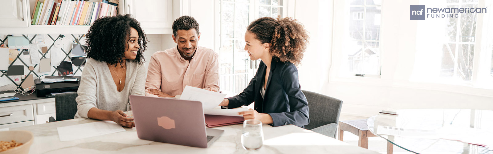 A couple goes over documents with a woman dressed in a suite in front of a laptop