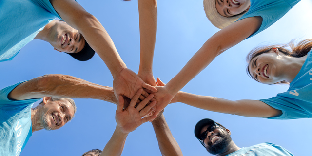 Group of happy diverse volunteers joining stacked hands together