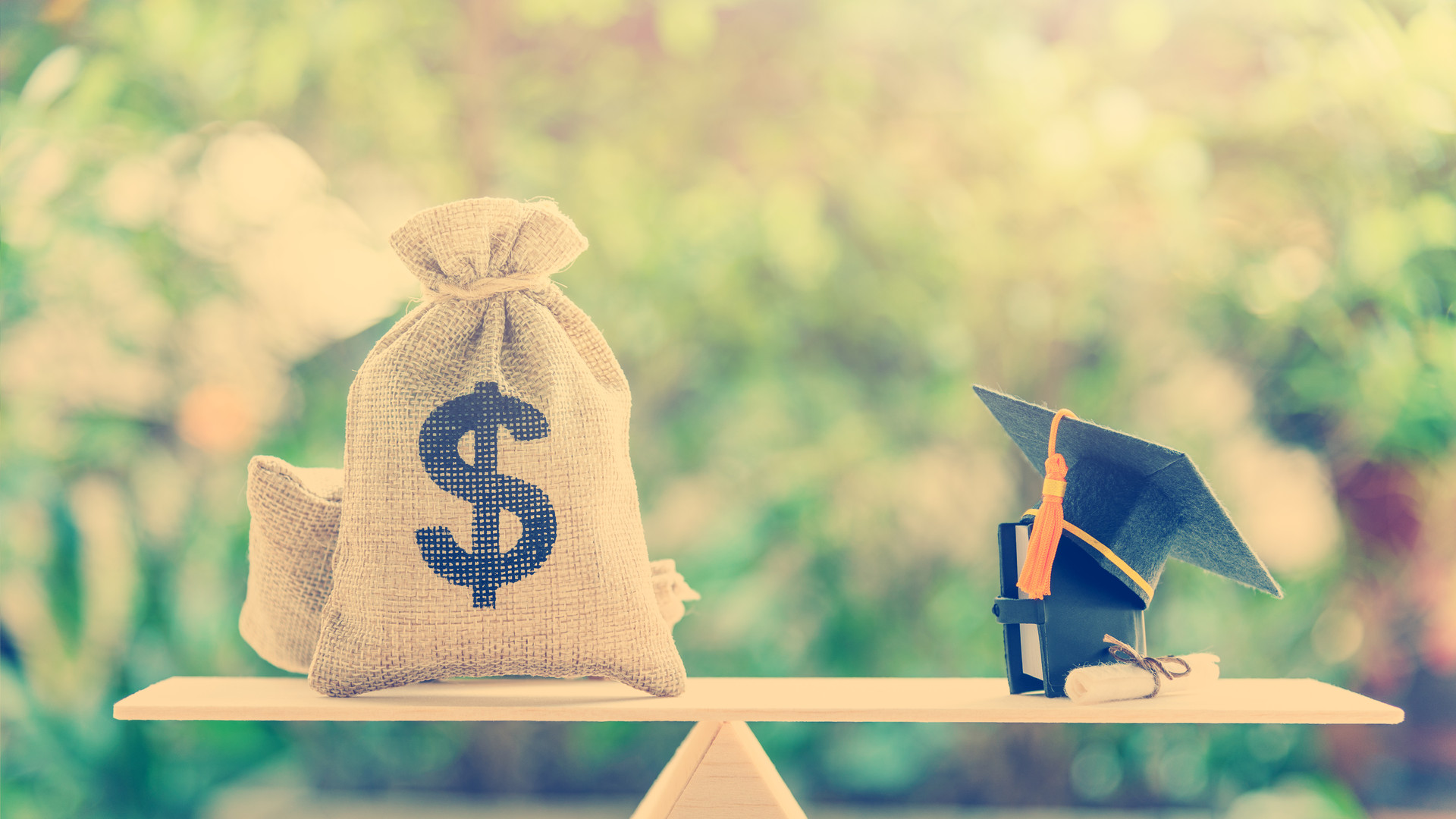 Money cost saving for goal and success in school, education concept : US dollar bills / cash in hessian bags, a black graduation cap or hat, a certificate / diploma and a book on simple balance scale.