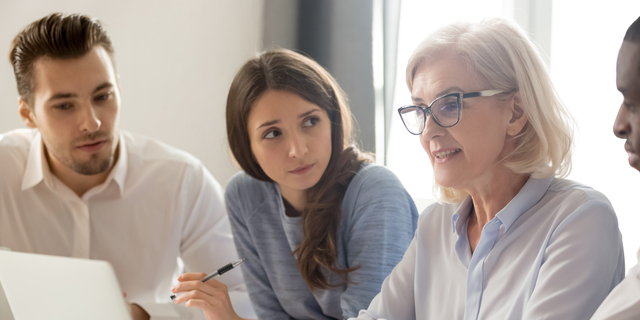 Focused young interns making notes listening to old female manager