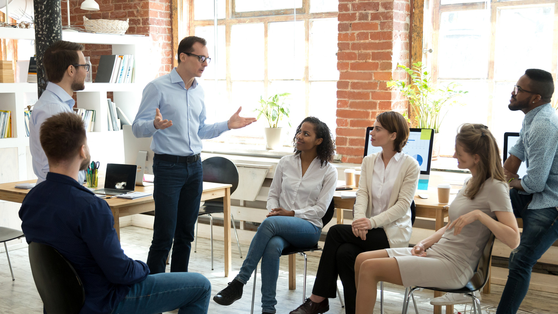 Diverse employees listening to male manager speaking at group meeting