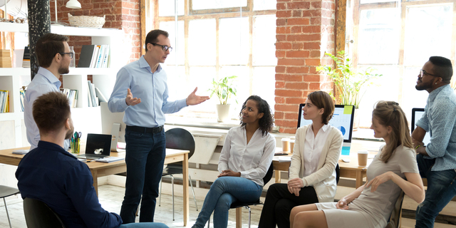 Diverse employees listening to male manager speaking at group meeting