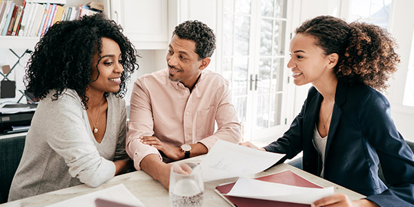 A Black man and Black woman sit smiling across from a Black business woman